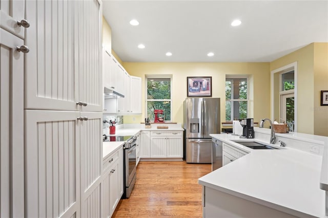 kitchen with recessed lighting, light countertops, under cabinet range hood, a sink, and appliances with stainless steel finishes
