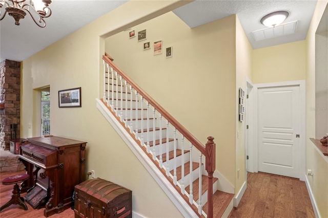 staircase featuring baseboards, visible vents, wood finished floors, and an inviting chandelier