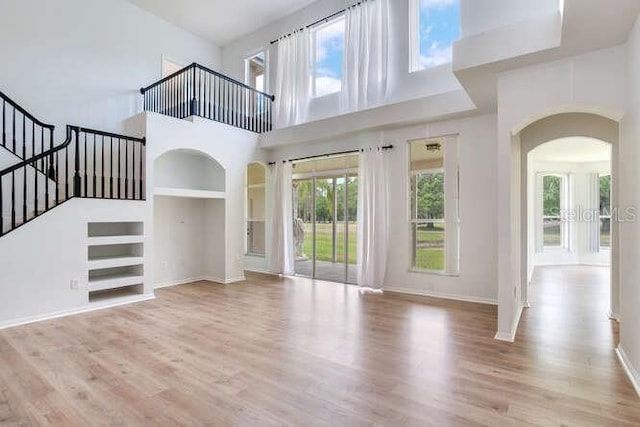 15906 Prince William Pl, Odessa, FL 33556 - unfurnished living room featuring arched walkways, a high ceiling, built in shelves, wood finished floors, and stairs