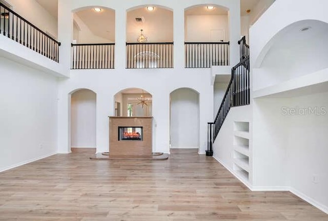 15906 Prince William Pl, Odessa, FL 33556 - unfurnished living room featuring built in features, wood finished floors, stairs, a multi sided fireplace, and a towering ceiling