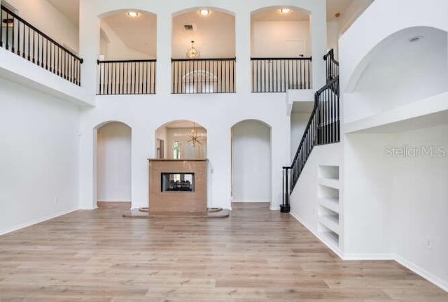 15906 Prince William Pl, Odessa, FL 33556 - unfurnished living room featuring built in shelves, wood finished floors, a multi sided fireplace, stairway, and a towering ceiling