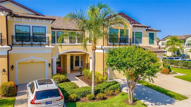 view of front of home with a balcony, an attached garage, stucco siding, driveway, and a shingled roof