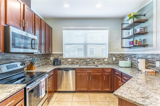 kitchen with stainless steel appliances, a sink, light tile patterned floors, light stone counters, and decorative backsplash