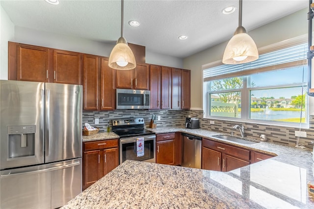 kitchen with appliances with stainless steel finishes, a sink, decorative backsplash, light stone countertops, and decorative light fixtures
