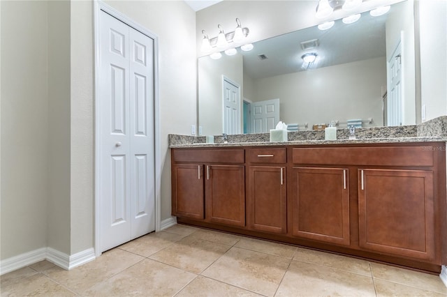 full bath featuring tile patterned flooring, double vanity, baseboards, and a closet