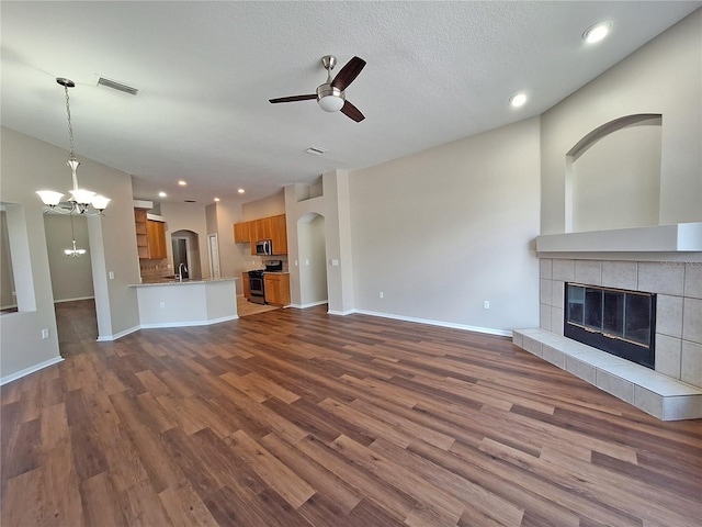 19855 Ellendale Dr, Land O Lakes, FL 34638 - unfurnished living room featuring ceiling fan, a chandelier, dark wood-type flooring, a tiled fireplace, and arched walkways