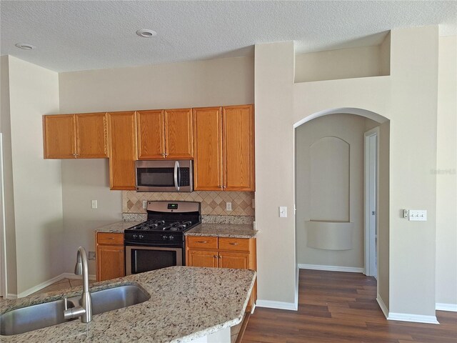 19855 Ellendale Dr, Land O Lakes, FL 34638 - kitchen with appliances with stainless steel finishes, a sink, arched walkways, dark wood-type flooring, and brown cabinets