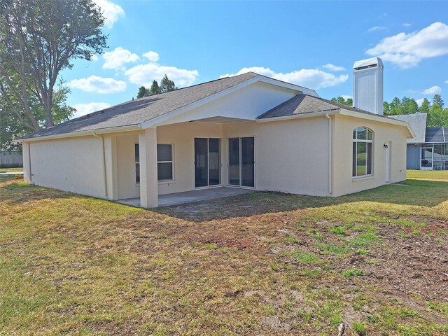 19855 Ellendale Dr, Land O Lakes, FL 34638 - back of house with a patio area, stucco siding, a chimney, a lawn, and roof with shingles