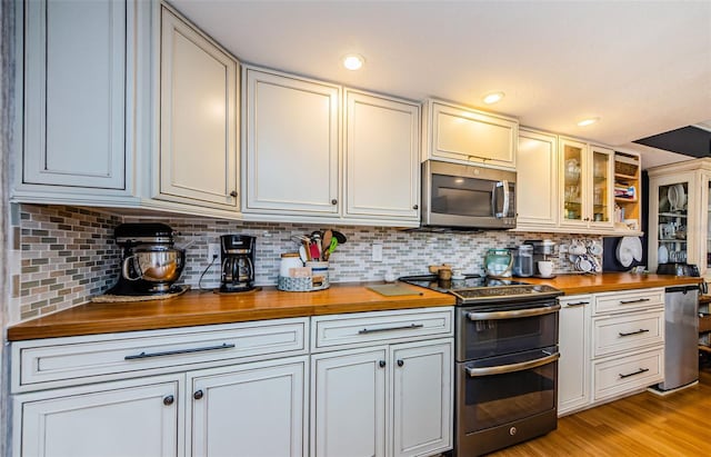 8210 Aquila St Unit 218, Port Richey, FL 34668 - kitchen with wooden counters, stainless steel appliances, backsplash, light wood-type flooring, and glass insert cabinets
