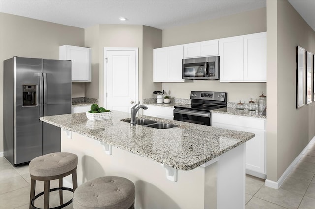 kitchen with a center island with sink, white cabinetry, a sink, light tile patterned floors, and stainless steel appliances