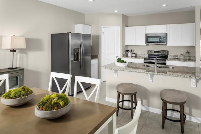 kitchen with white cabinets, light stone counters, a kitchen breakfast bar, stainless steel appliances, and light tile patterned floors