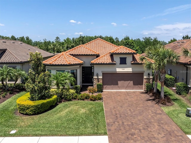 mediterranean / spanish-style home featuring a tiled roof, a garage, decorative driveway, a front lawn, and stucco siding