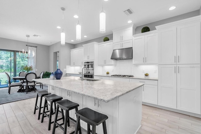 kitchen featuring visible vents, a center island with sink, a sink, white cabinets, and under cabinet range hood