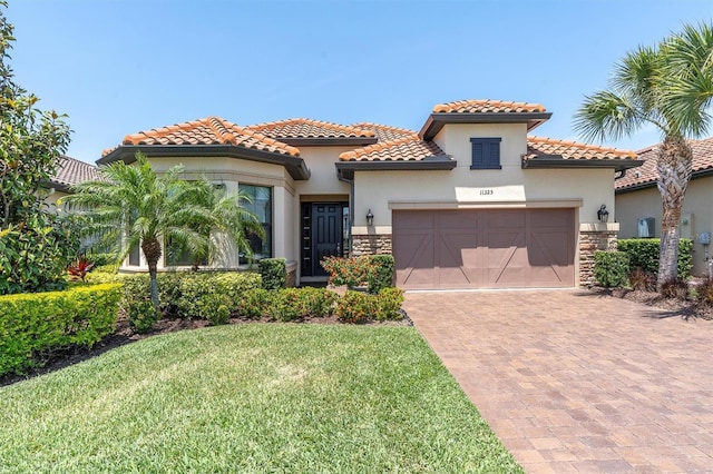 mediterranean / spanish-style house featuring decorative driveway, a garage, stucco siding, and stone siding