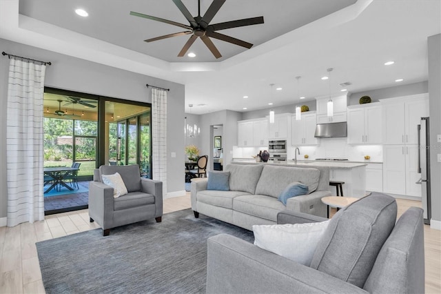 living area with recessed lighting, baseboards, ceiling fan, and a tray ceiling