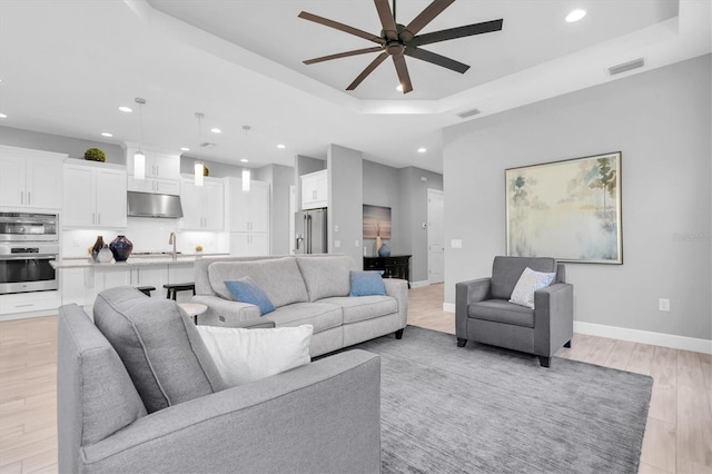 living room featuring recessed lighting, a ceiling fan, light wood-type flooring, a tray ceiling, and visible vents