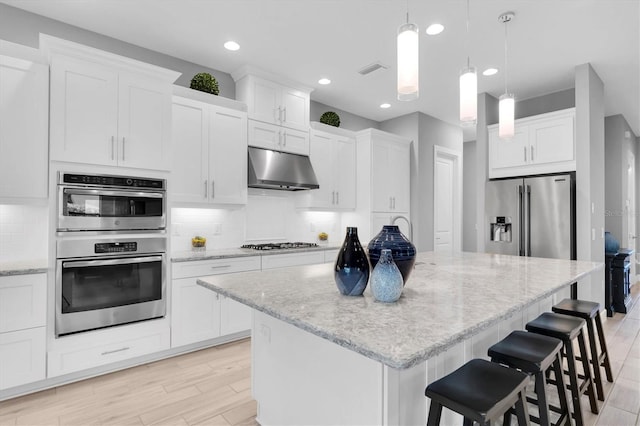 kitchen with decorative backsplash, appliances with stainless steel finishes, a center island, white cabinets, and under cabinet range hood