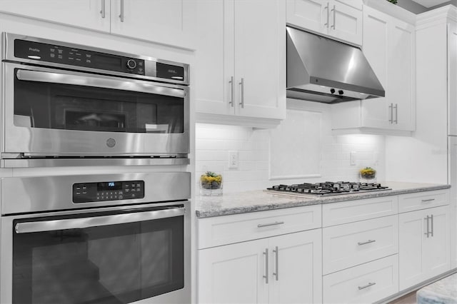 kitchen featuring appliances with stainless steel finishes, tasteful backsplash, light stone counters, white cabinets, and under cabinet range hood