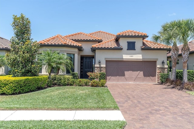 mediterranean / spanish-style house with an attached garage, stone siding, stucco siding, decorative driveway, and a tiled roof