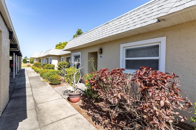 property entrance with mansard roof, roof with shingles, and stucco siding