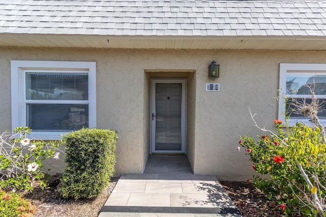 doorway to property with roof with shingles and stucco siding