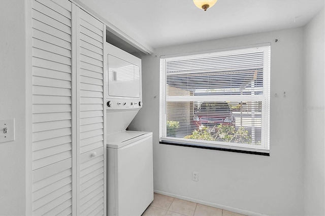 laundry area with light tile patterned floors, baseboards, stacked washer / drying machine, and laundry area