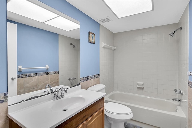 bathroom with visible vents, vanity, shower / bathtub combination, toilet, and tile walls