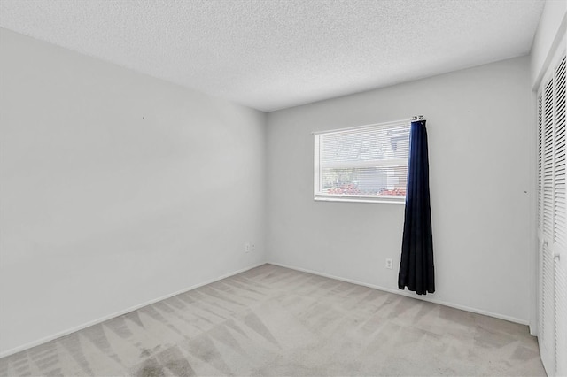spare room featuring baseboards, a textured ceiling, and light colored carpet