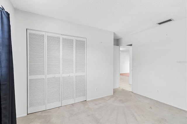 unfurnished bedroom with visible vents, a textured ceiling, carpet, and a closet