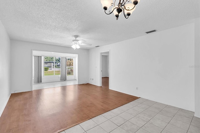 spare room with light wood-style floors, ceiling fan with notable chandelier, a textured ceiling, and visible vents