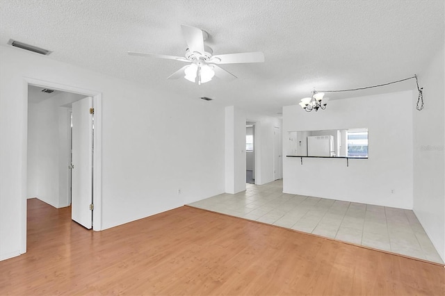 unfurnished living room with ceiling fan with notable chandelier, light wood finished floors, a textured ceiling, and visible vents