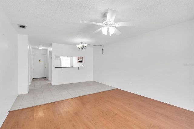 interior space with ceiling fan with notable chandelier, light wood finished floors, a textured ceiling, and visible vents