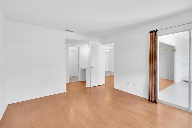 unfurnished bedroom featuring visible vents, light wood finished floors, a spacious closet, and a closet