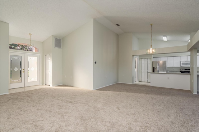 unfurnished living room with light colored carpet, a chandelier, high vaulted ceiling, and visible vents