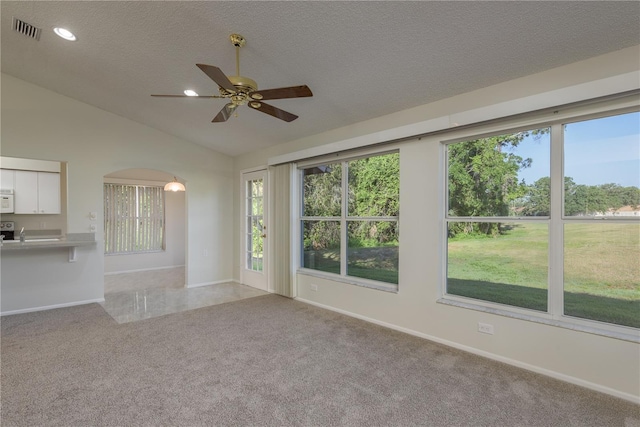 unfurnished living room with ceiling fan, a textured ceiling, light colored carpet, visible vents, and vaulted ceiling