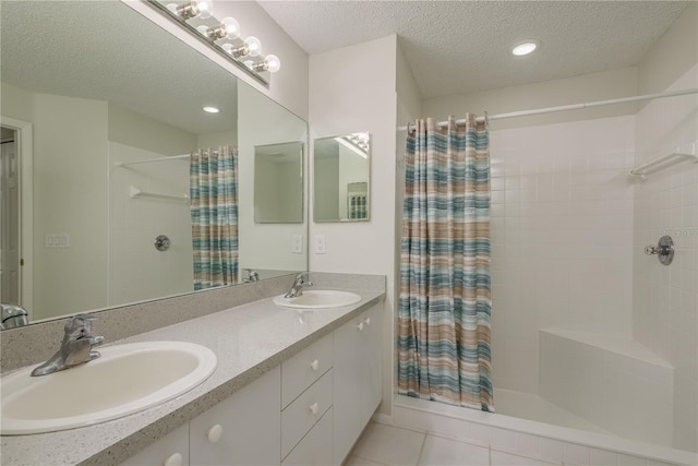 bathroom with a textured ceiling, a tile shower, a sink, and tile patterned flooring