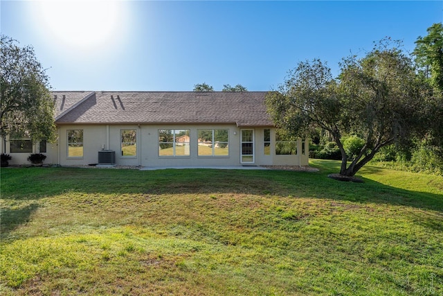 back of property featuring central AC, roof with shingles, stucco siding, and a yard