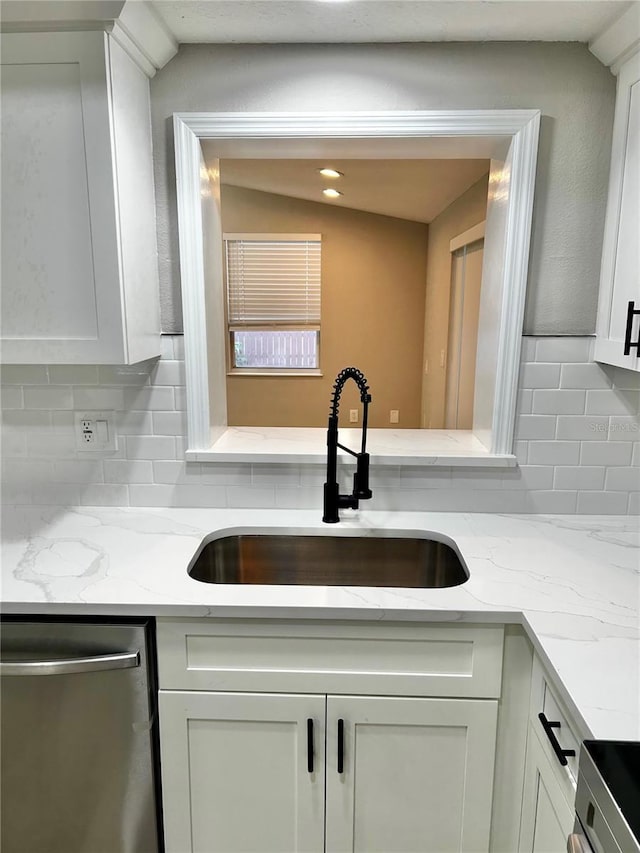 kitchen with white cabinets, light stone countertops, a sink, stainless steel appliances, and tasteful backsplash