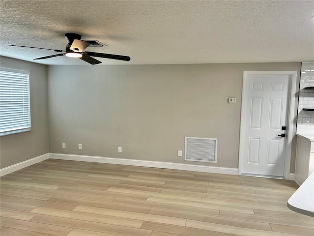 unfurnished room with a textured ceiling, a ceiling fan, baseboards, light wood-type flooring, and visible vents
