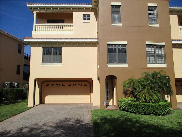 view of front facade with decorative driveway, central AC, a balcony, an attached garage, and stucco siding