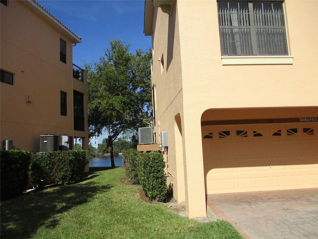 view of side of home featuring a garage, stucco siding, a yard, and a water view