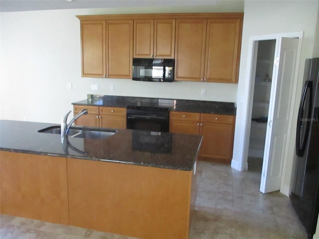 kitchen featuring a sink, brown cabinetry, black appliances, and dark stone countertops