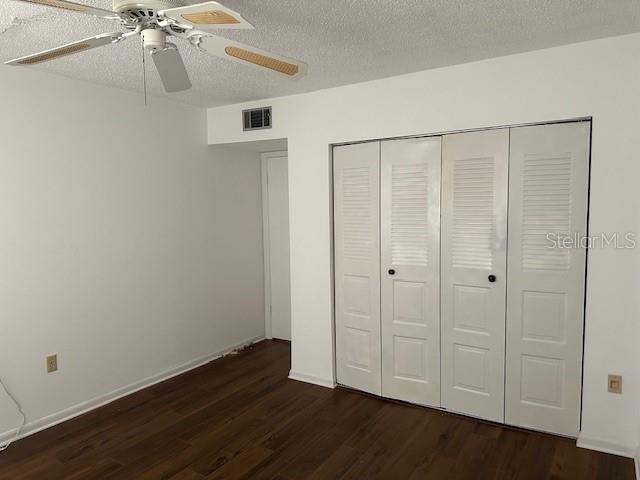 840 Virginia St Unit 202, Dunedin, FL 34698 - unfurnished bedroom with ceiling fan, dark wood-style flooring, a textured ceiling, visible vents, and a closet