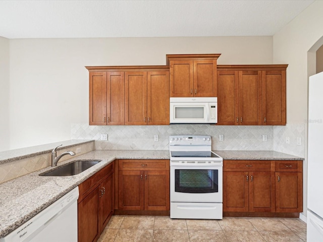 kitchen with decorative backsplash, light stone counters, a sink, and white appliances