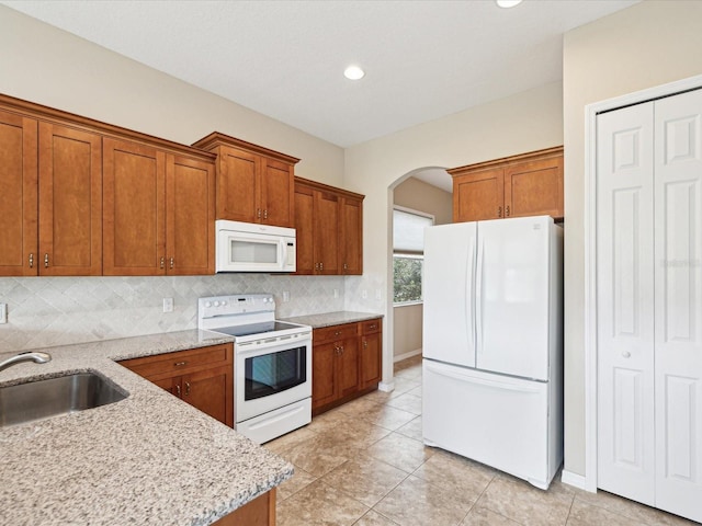 kitchen featuring a sink, brown cabinetry, white appliances, and arched walkways