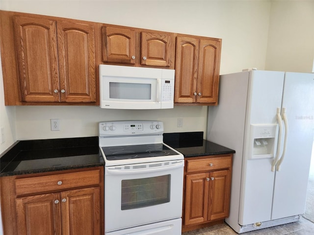 kitchen with brown cabinetry, dark stone countertops, and white appliances