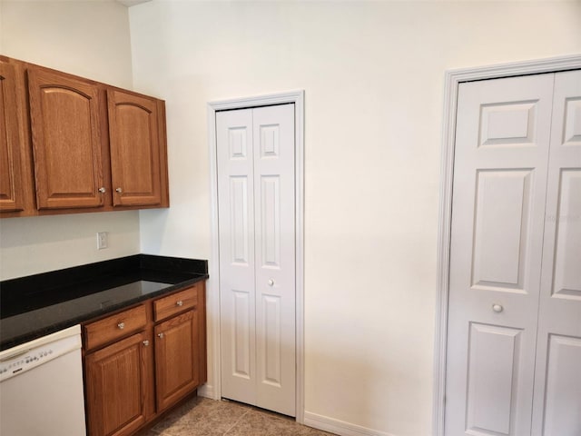 kitchen featuring white dishwasher, dark countertops, brown cabinets, and light tile patterned flooring