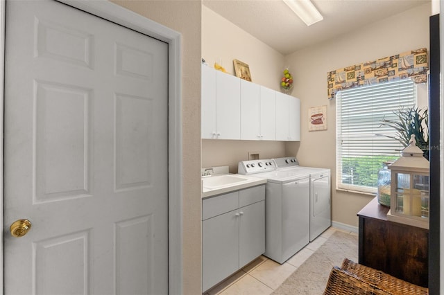 clothes washing area featuring cabinet space, washing machine and clothes dryer, a sink, baseboards, and light tile patterned floors