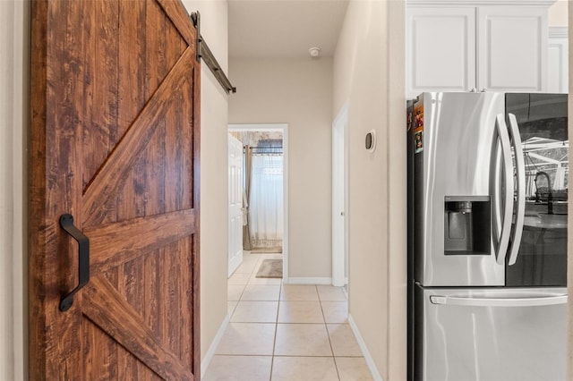 hall featuring baseboards, a barn door, and light tile patterned flooring