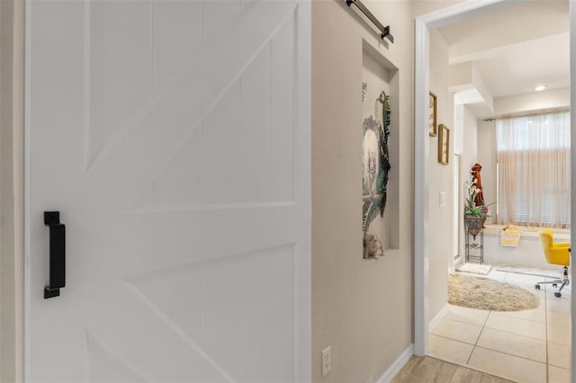 corridor featuring baseboards, a barn door, and light wood-type flooring